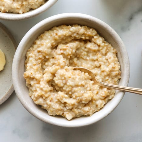 two white bowls filled with instant pot steel cut oats and a spoon.