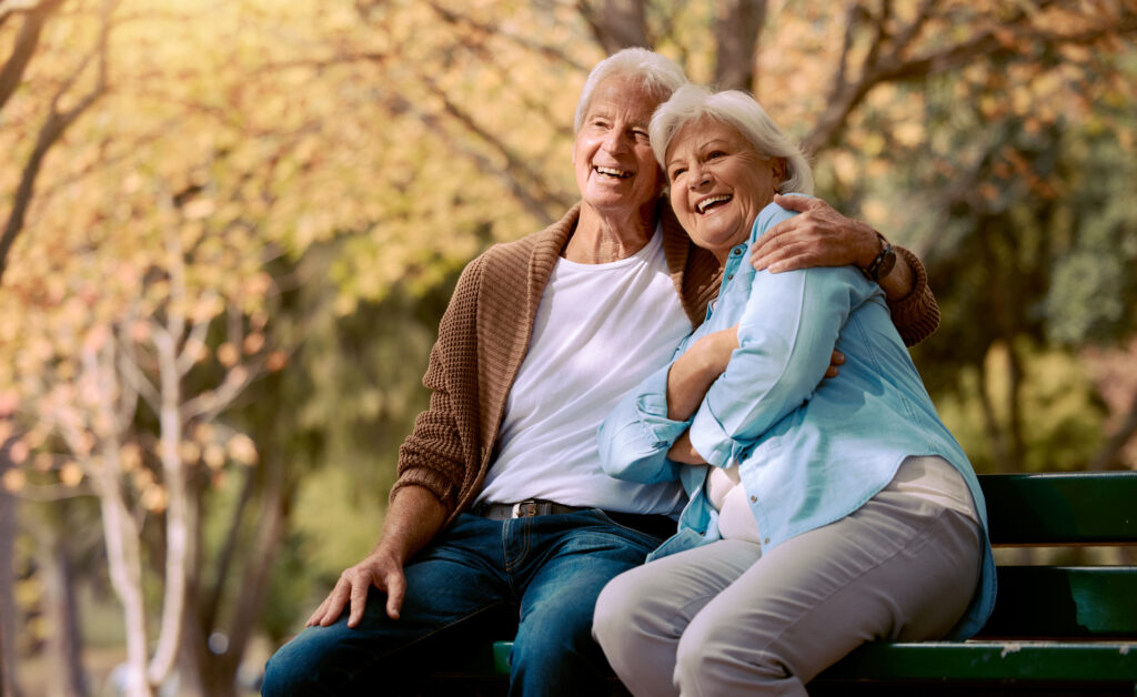 Senior couple, park bench and happy while sitting together in retirement for freedom, peace and calm with a smile and happiness in nature. Old man and woman outdoor to relax while on vacation