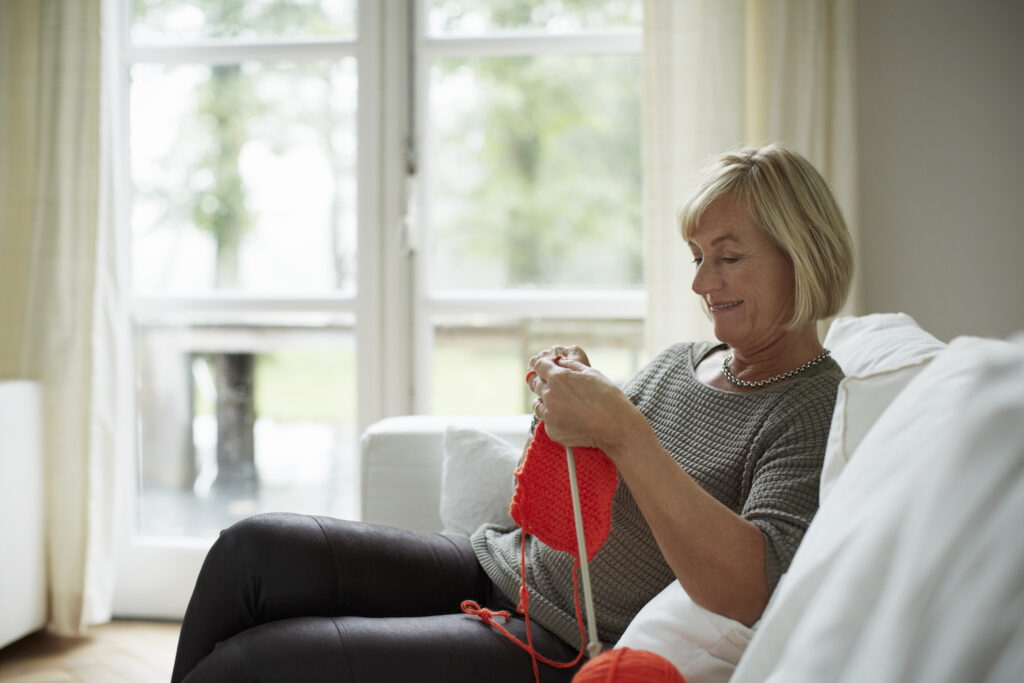 Senior woman knitting while sitting on sofa in house