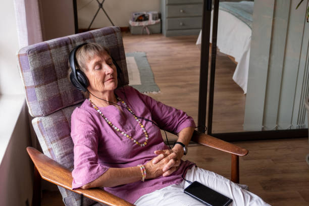 Senior woman sits and relaxes with music in her ears An elderly woman relaxes, she has earphones on and listens to some music. Senior woman enjoying her retirement years. seniors listening to music stock pictures, royalty-free photos & images