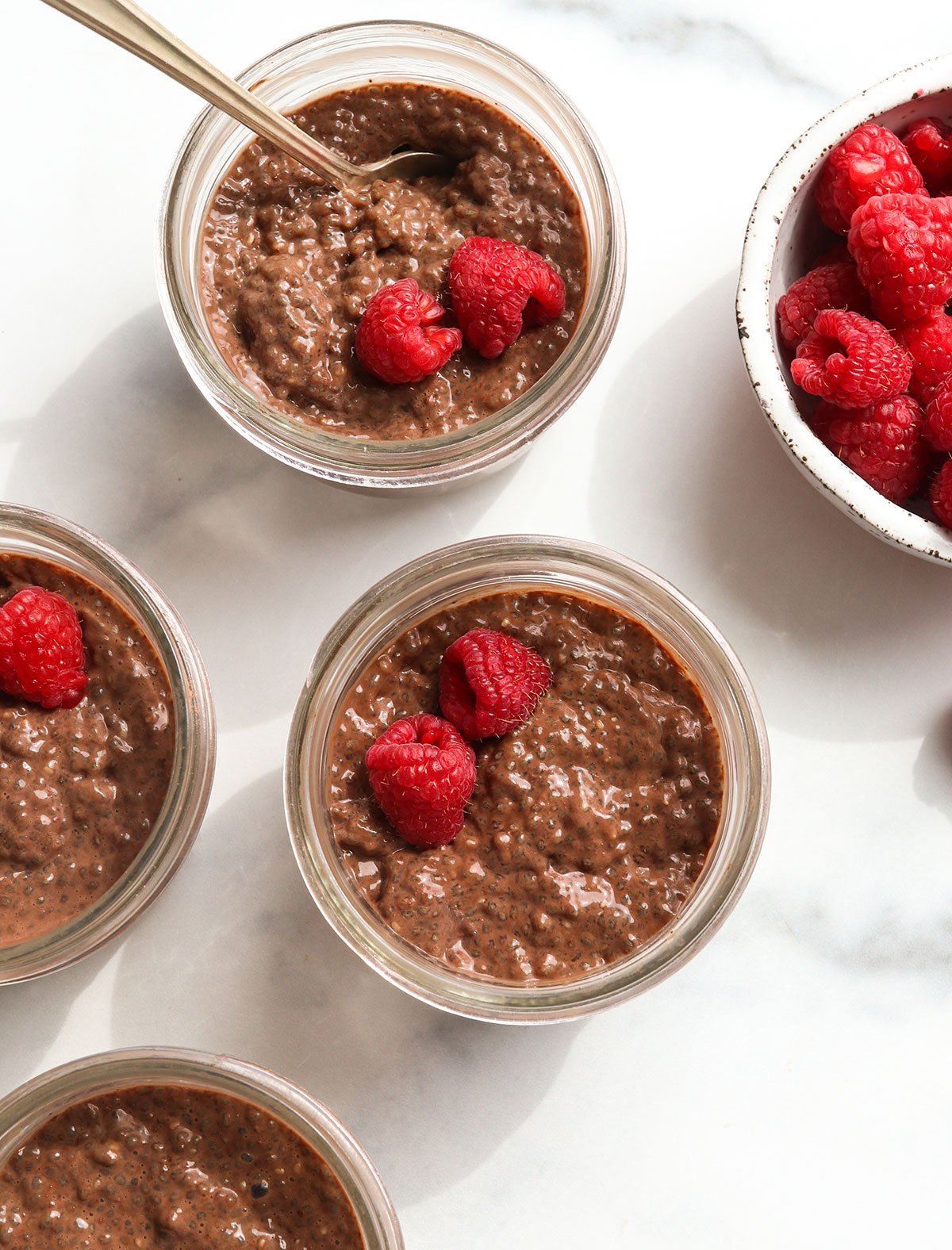 4 jars of chocolate chia pudding topped with fresh raspberries.